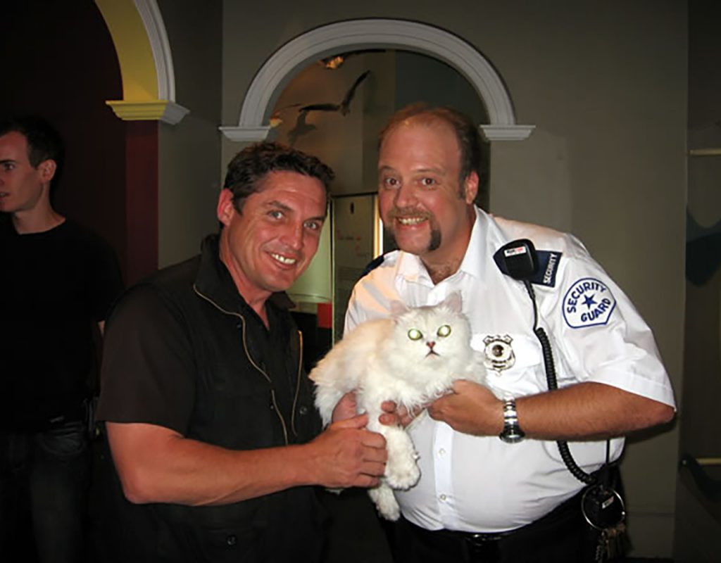 two men posing for a photo with a cat